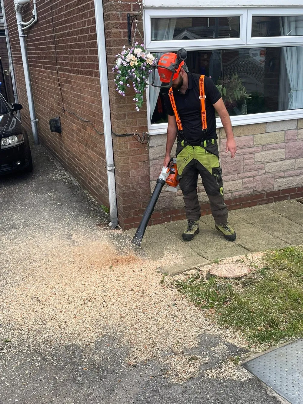 A man is using a leaf blower on the sidewalk.